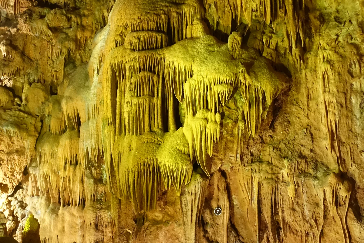 Layered mineral formations on an illuminated wall inside the Mira de Aire caves.