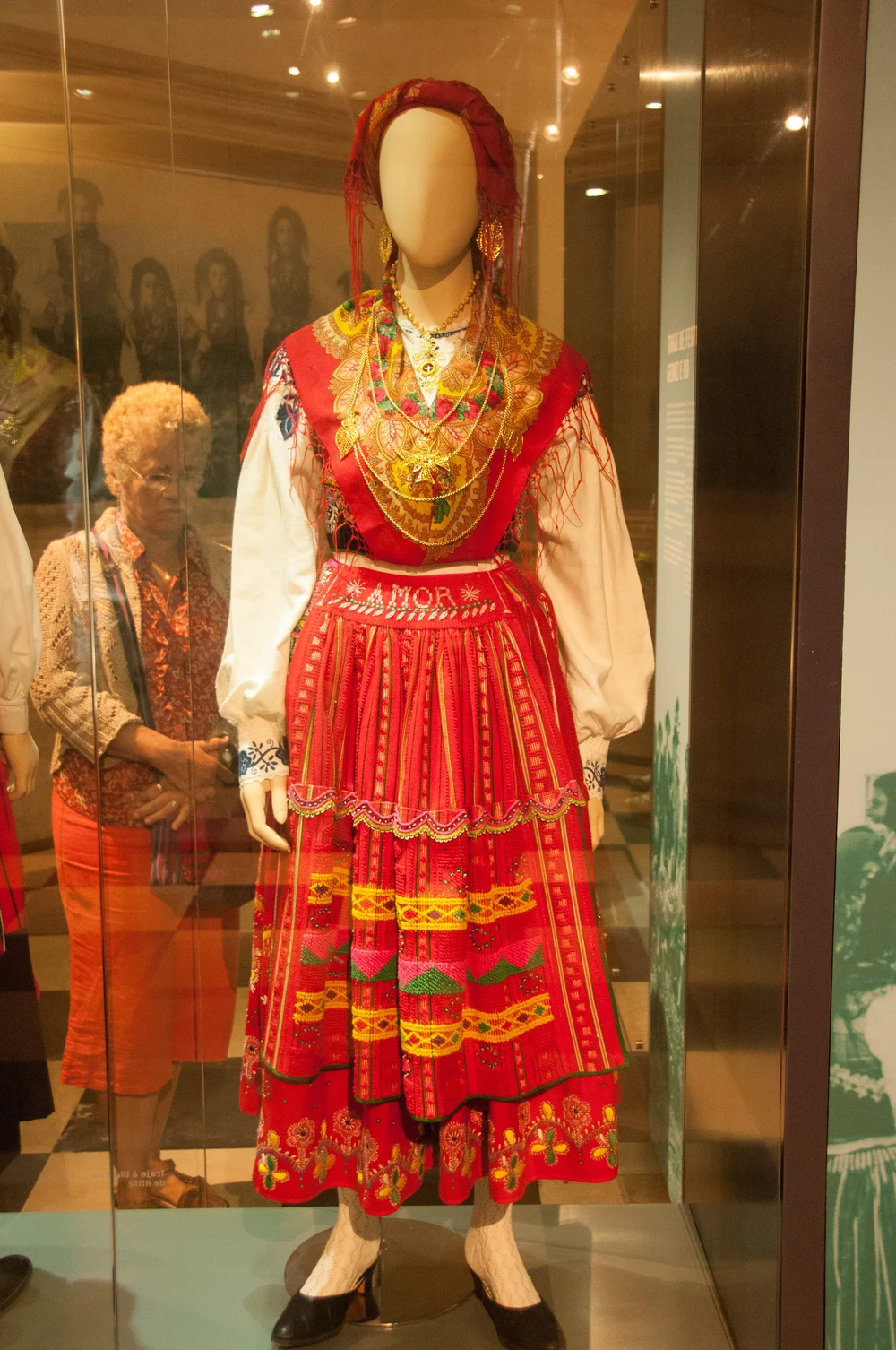 A museum mannequin in a red Viana outfit with a patterned apron, scarves and gold jewellery.