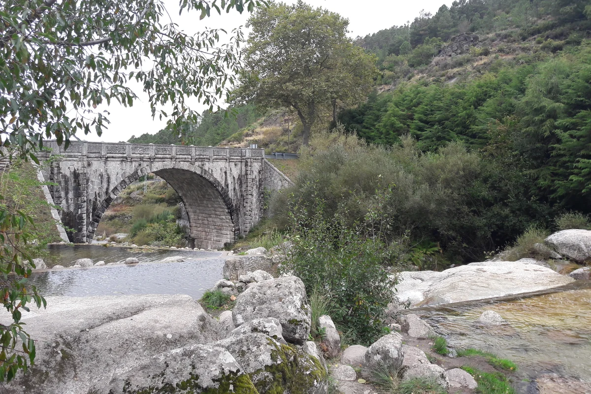 Stone pools below an arched bridge at Loriga, with wooded slopes behind.
